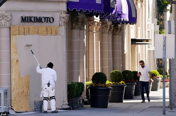 6. Một công nhân sơn lên các tấm ván đã đóng lên cửa kính tại một cửa hàng trang sức Mikimoto vào 30/10 ở Beverly Hills, Los Angeles.