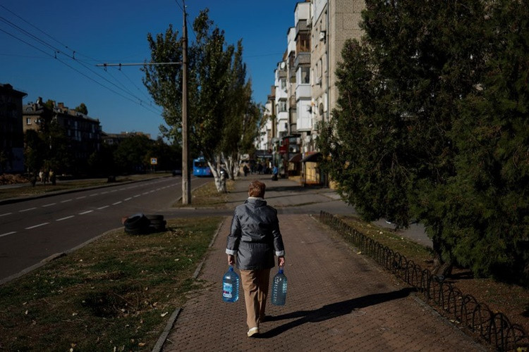 Người phụ nữ trở về nhà sau khi đã lấy được hai chai nước sạch do xe bồn chở tới ở Mykolaiv hôm 16/10. Ảnh: Reuters.