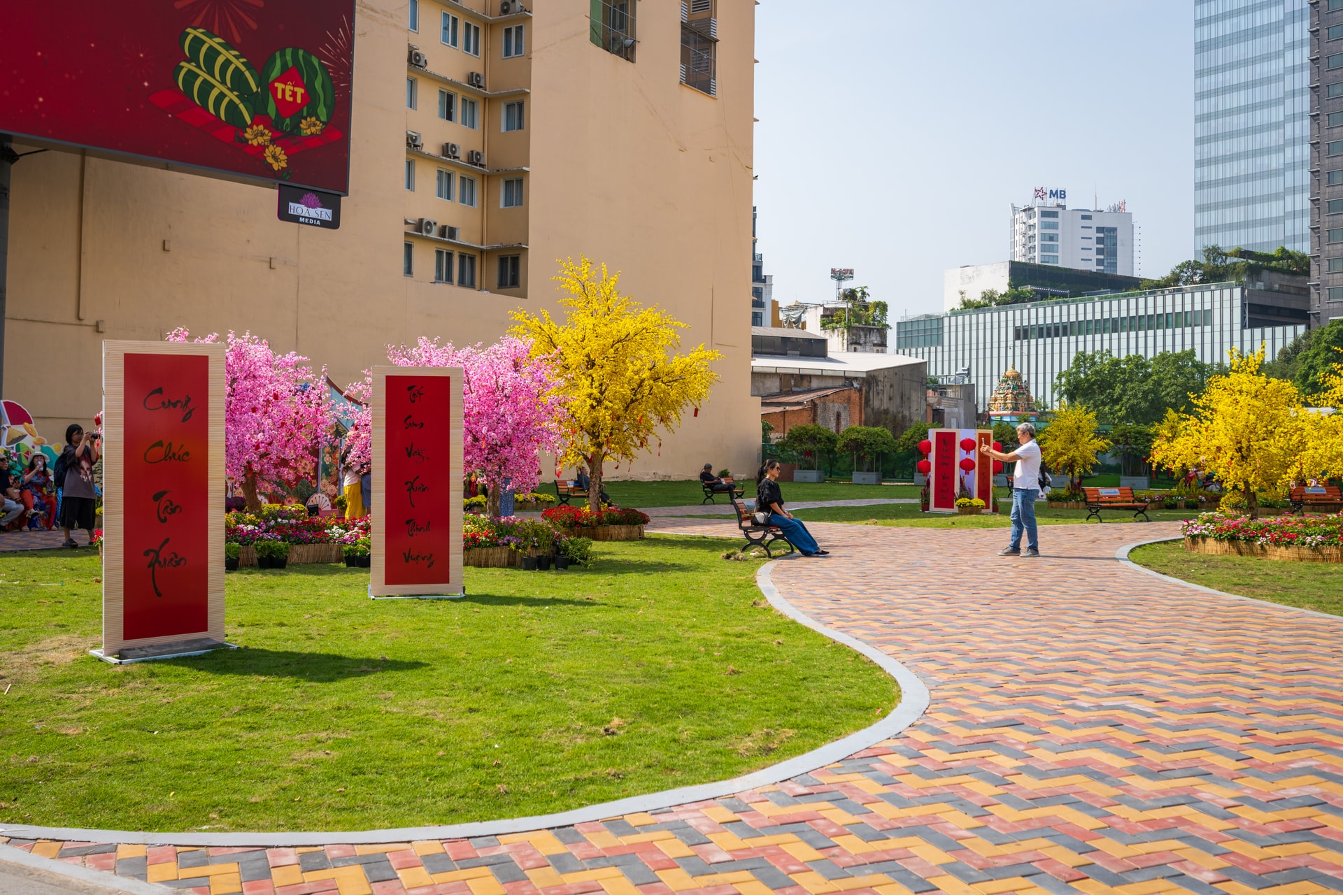 Những lối đi lát tạm, bồn hoa uốn cong mềm mại, tiểu cảnh mai đào đan xen giữa nền cỏ non khiến không gian vốn bị quây tôn thường trực nay trở nên gần gũi.